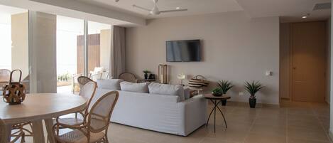 A modern living room with a sofa, dining table, chairs, and a TV mounted on the wall.