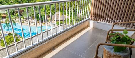 A balcony with a view of a pool and ocean, wicker furniture, and a stone column.