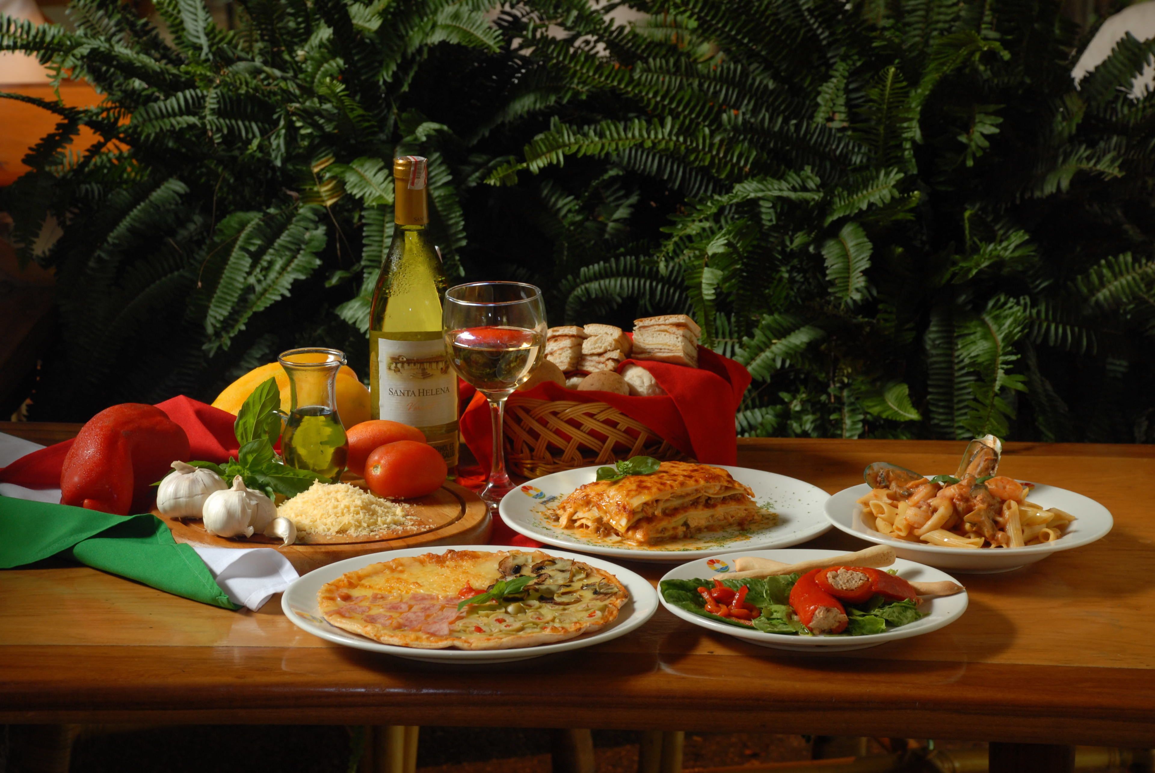 A table with various dishes, including pizza, pasta, and bread, along with condiments and a bottle of wine.