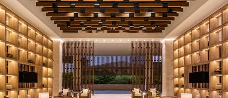 A modern lobby with a wooden ceiling, comfortable seating, and a large TV screen.