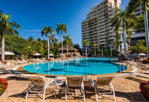 Una piscina con sillas de descanso y palmeras, rodeada por un edificio alto.