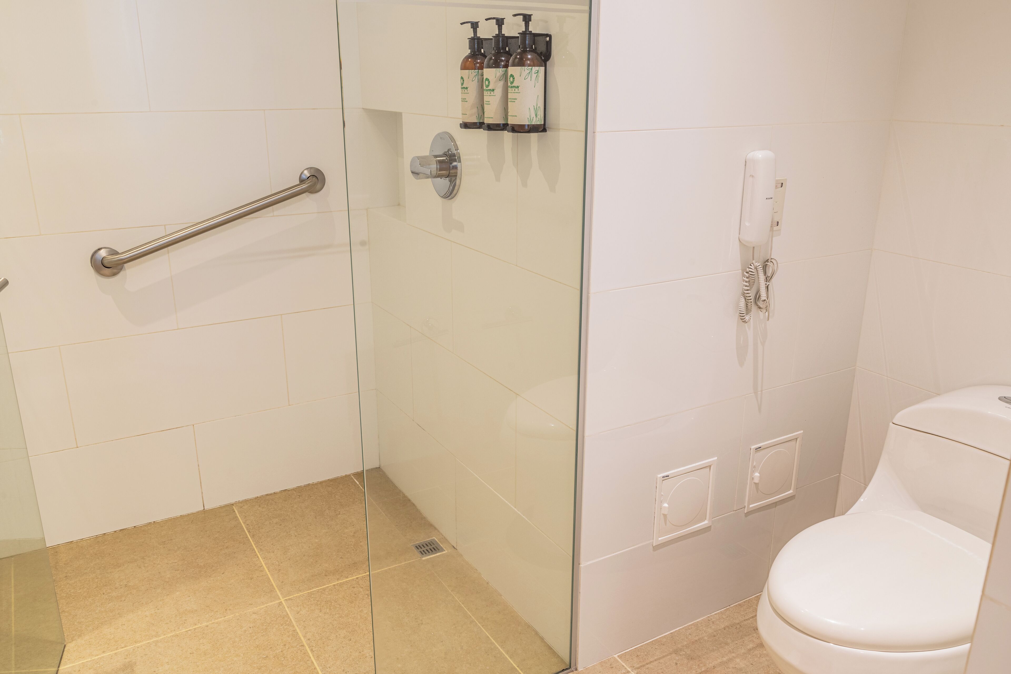 A bathroom with a glass shower enclosure, a white toilet, and a hand dryer.
