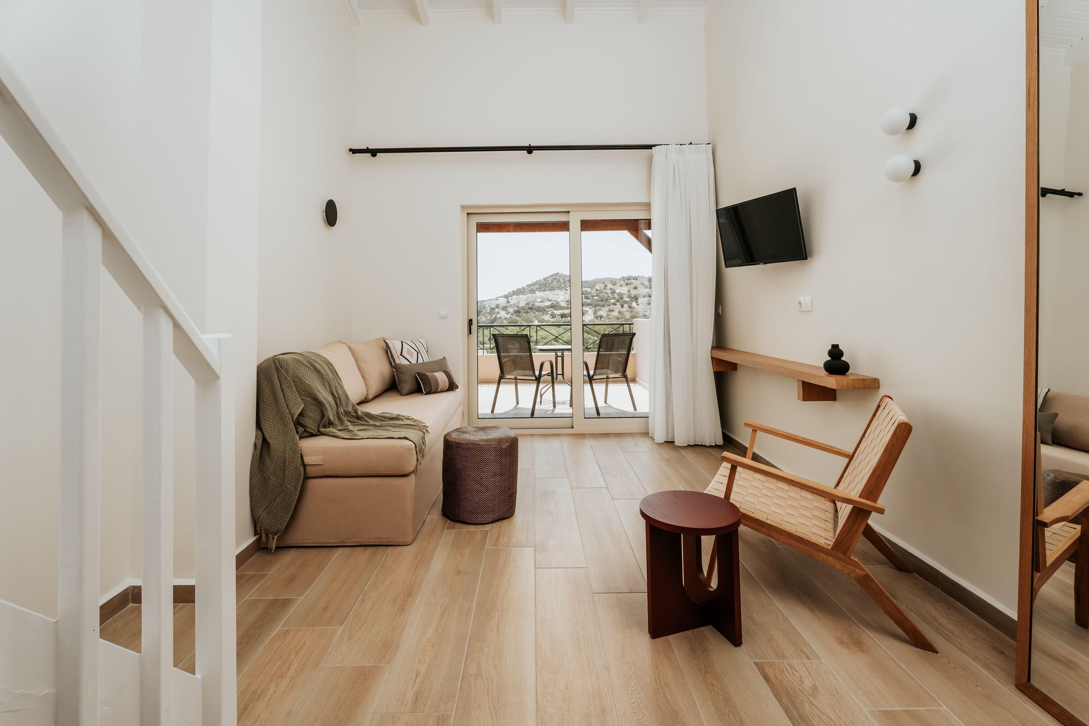 A modern living room with a sofa, a wooden chair, a small table, and a TV mounted on the wall.