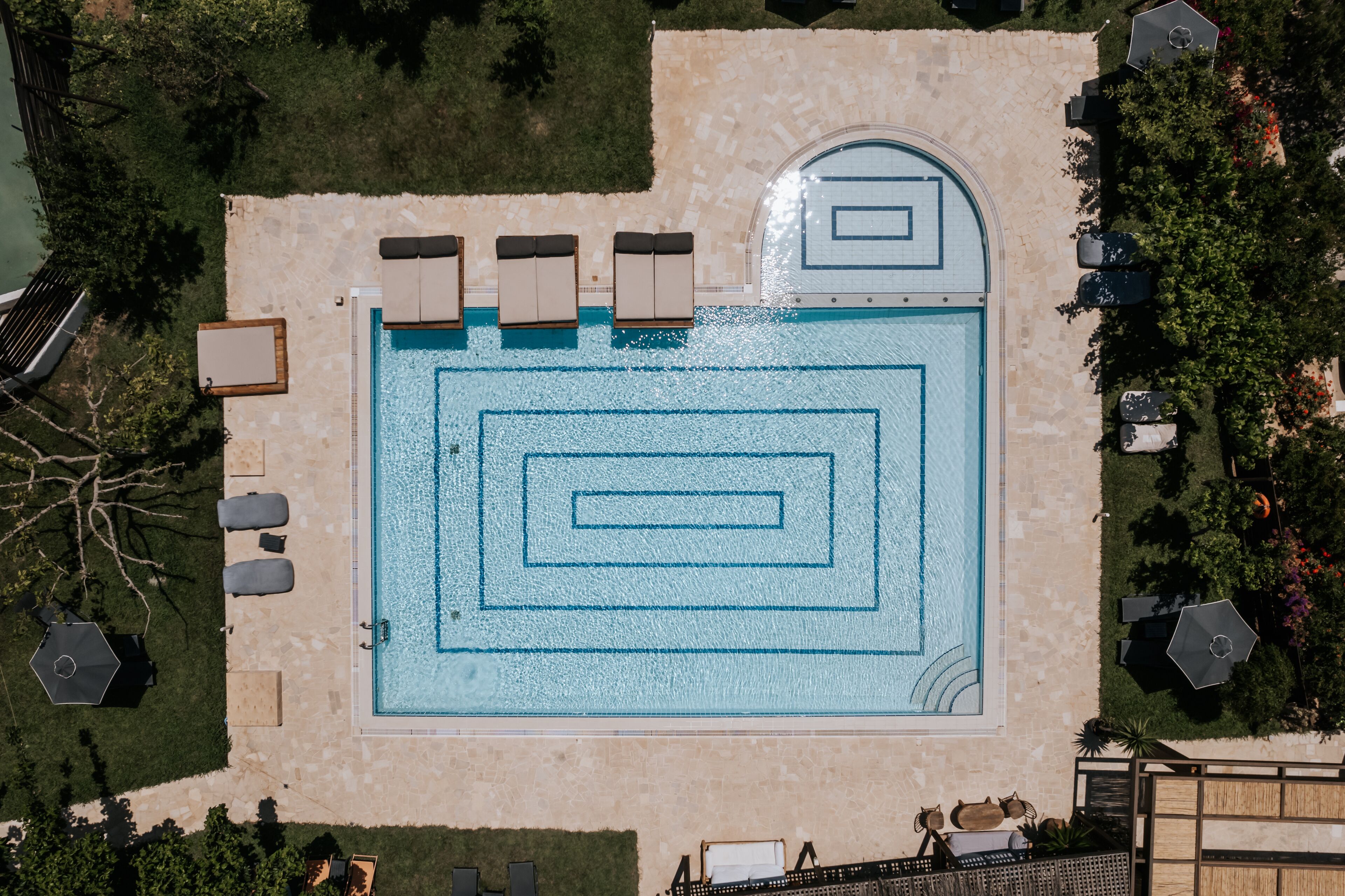 An aerial view of a swimming pool with geometric patterns, surrounded by lounge chairs and a stone deck.