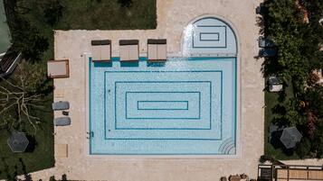 An aerial view of a swimming pool with geometric patterns, surrounded by lounge chairs and a stone deck.