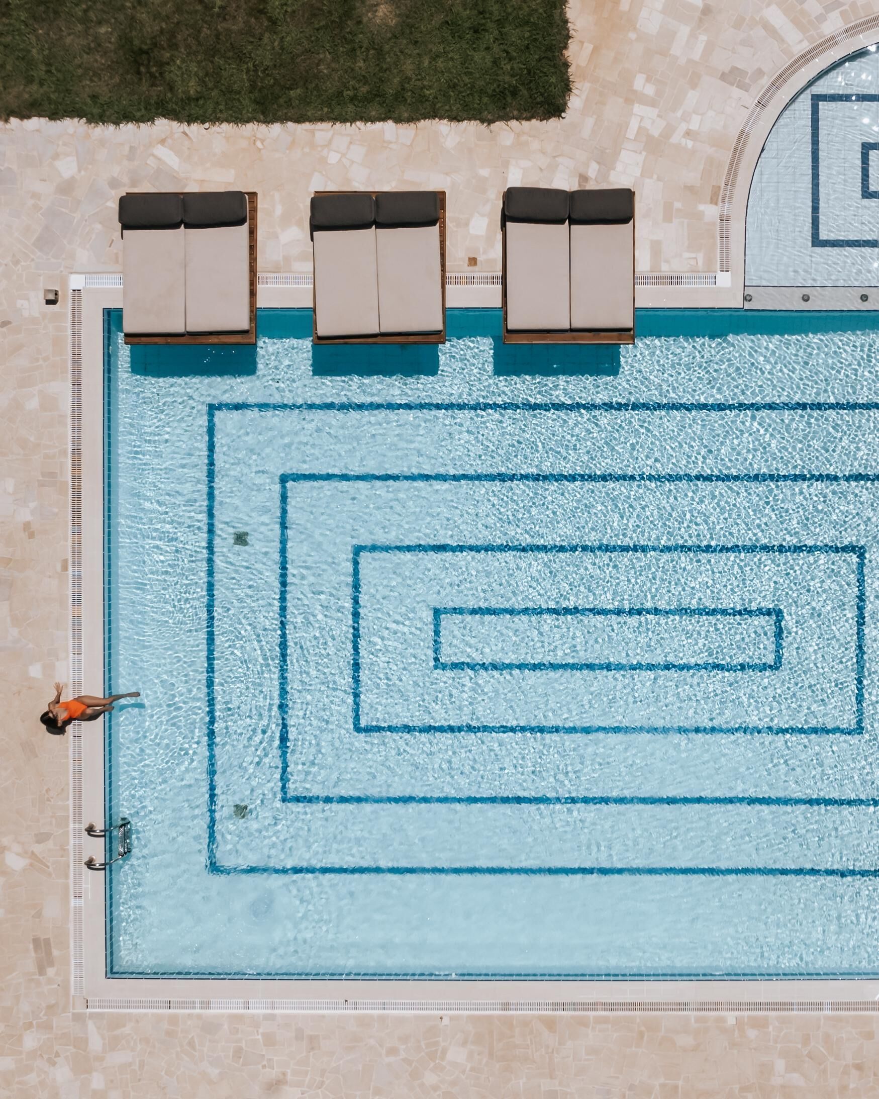 An aerial view of a swimming pool with multiple lounge chairs and a person swimming.