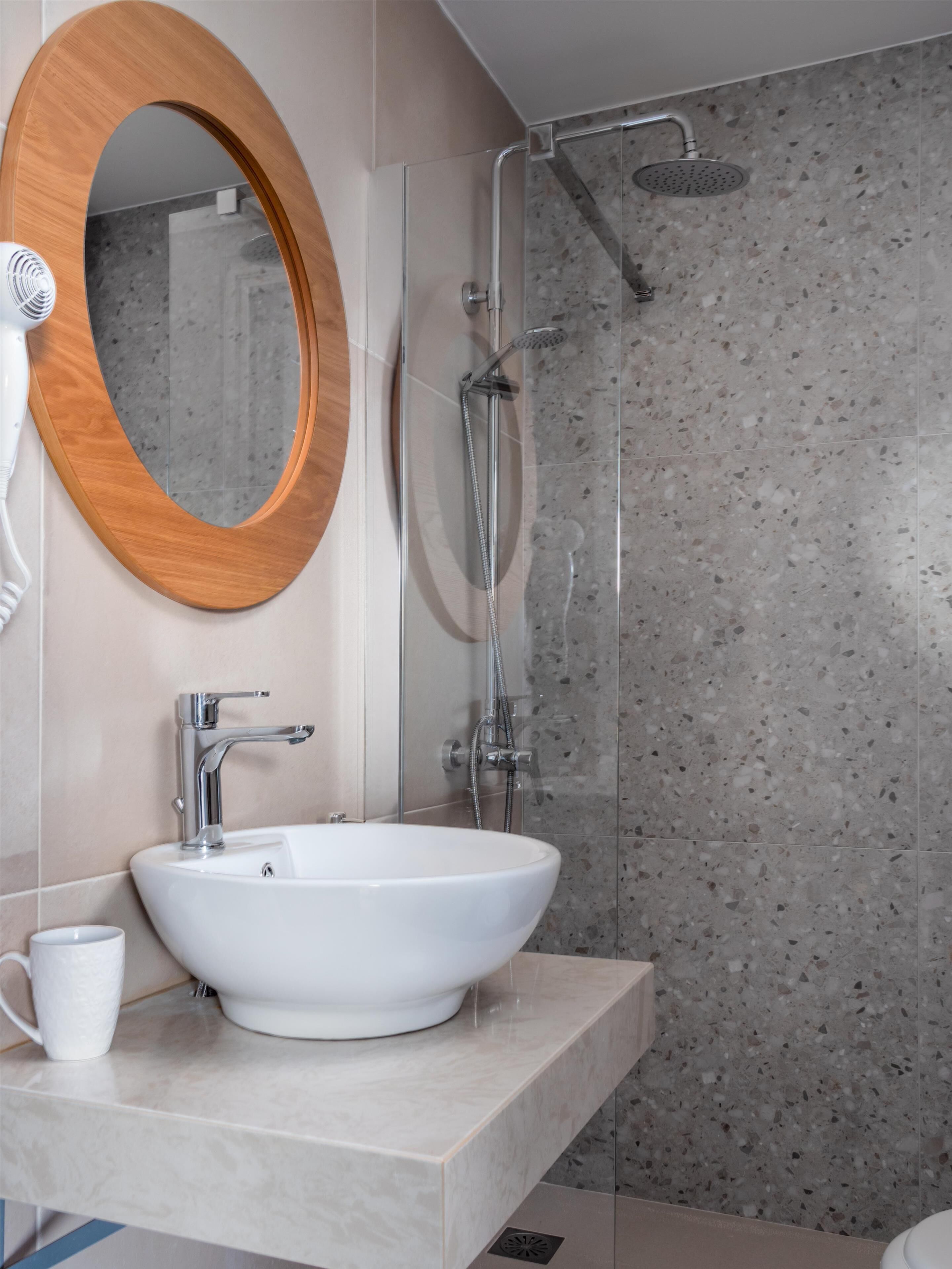 Un baño moderno con lavamanos independiente, cabina de ducha y un espejo grande con marco de madera.