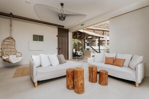Una sala moderna con dos sofás blancos, un sillón colgante y taburetes de madera.