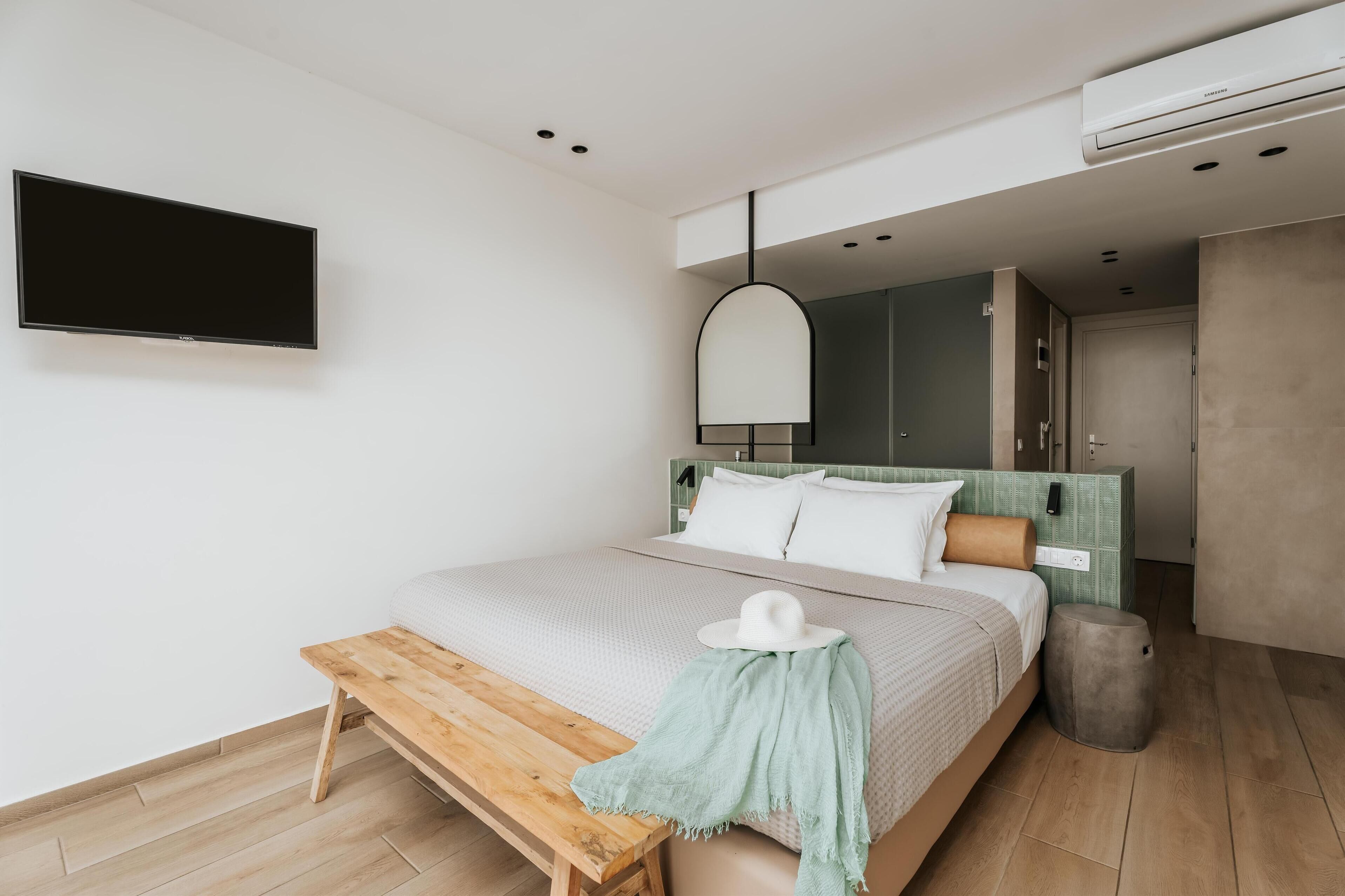 Un dormitorio moderno con cama, una banca, televisor y armario.