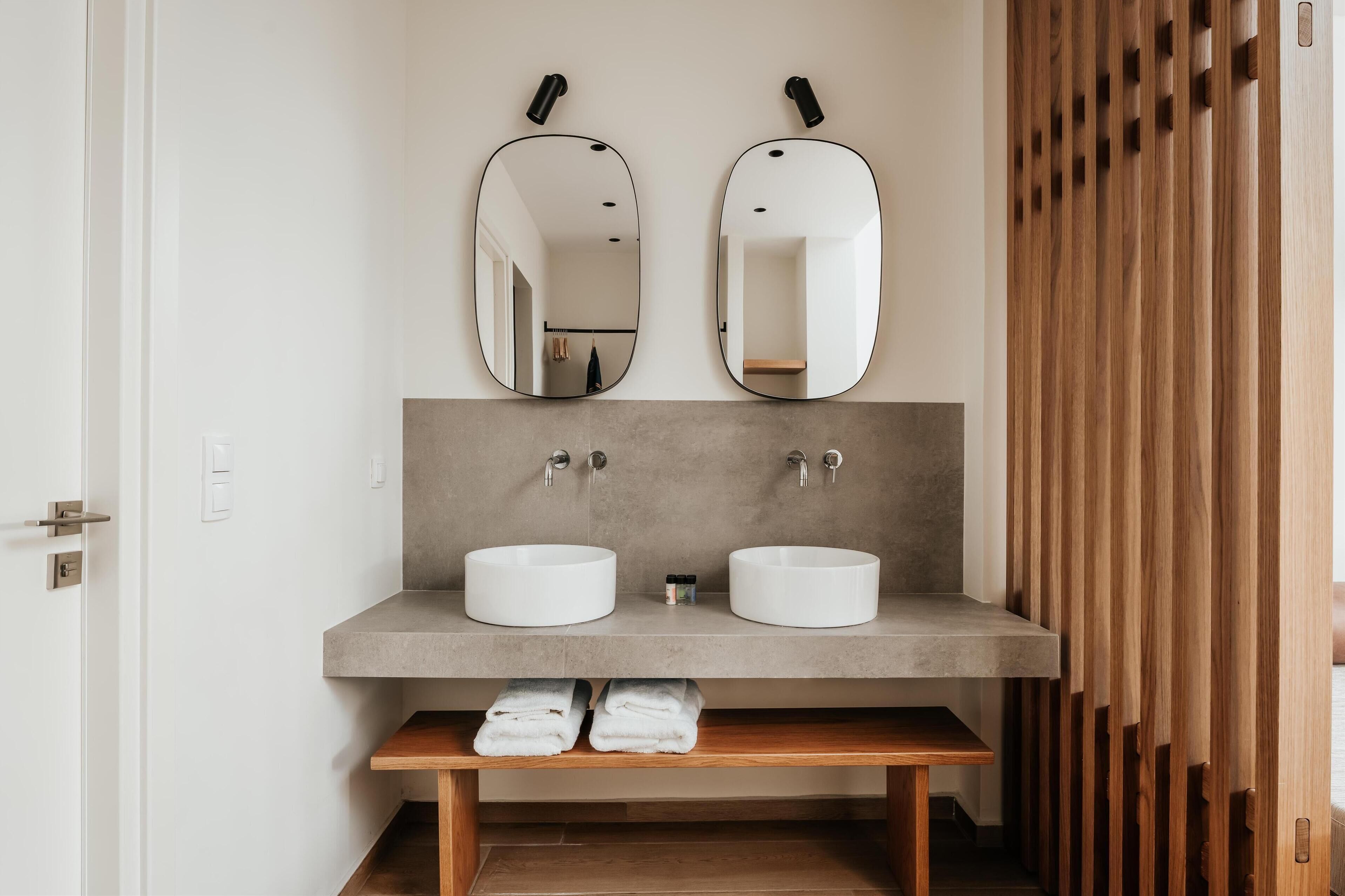 Un baño moderno con dos lavamanos, un banco con toallas y listones de madera a la derecha.