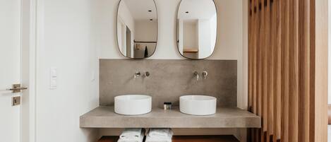 Un baño moderno con dos lavamanos, un banco con toallas y listones de madera a la derecha.