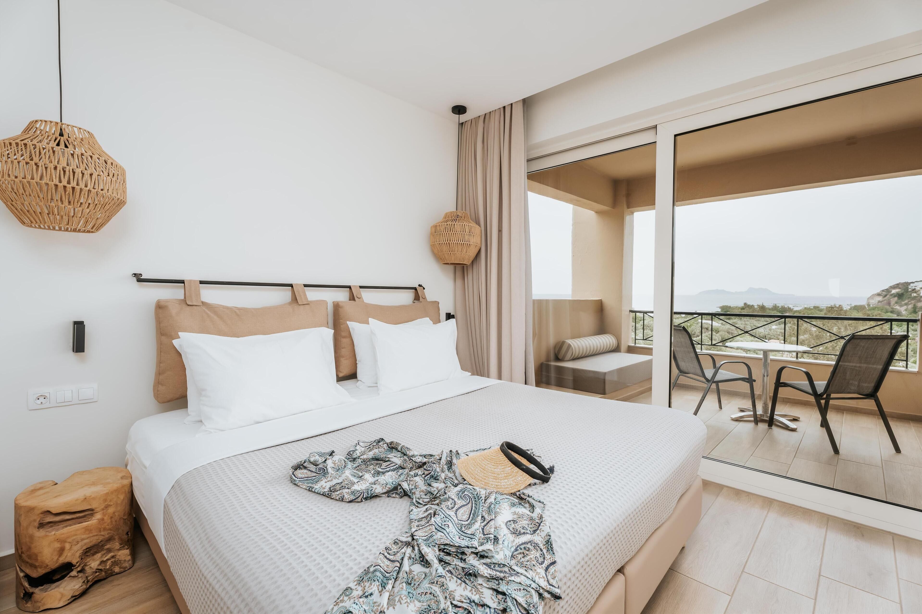 A modern hotel room with a large bed, a balcony with a table and chairs, and a view of the cityscape.