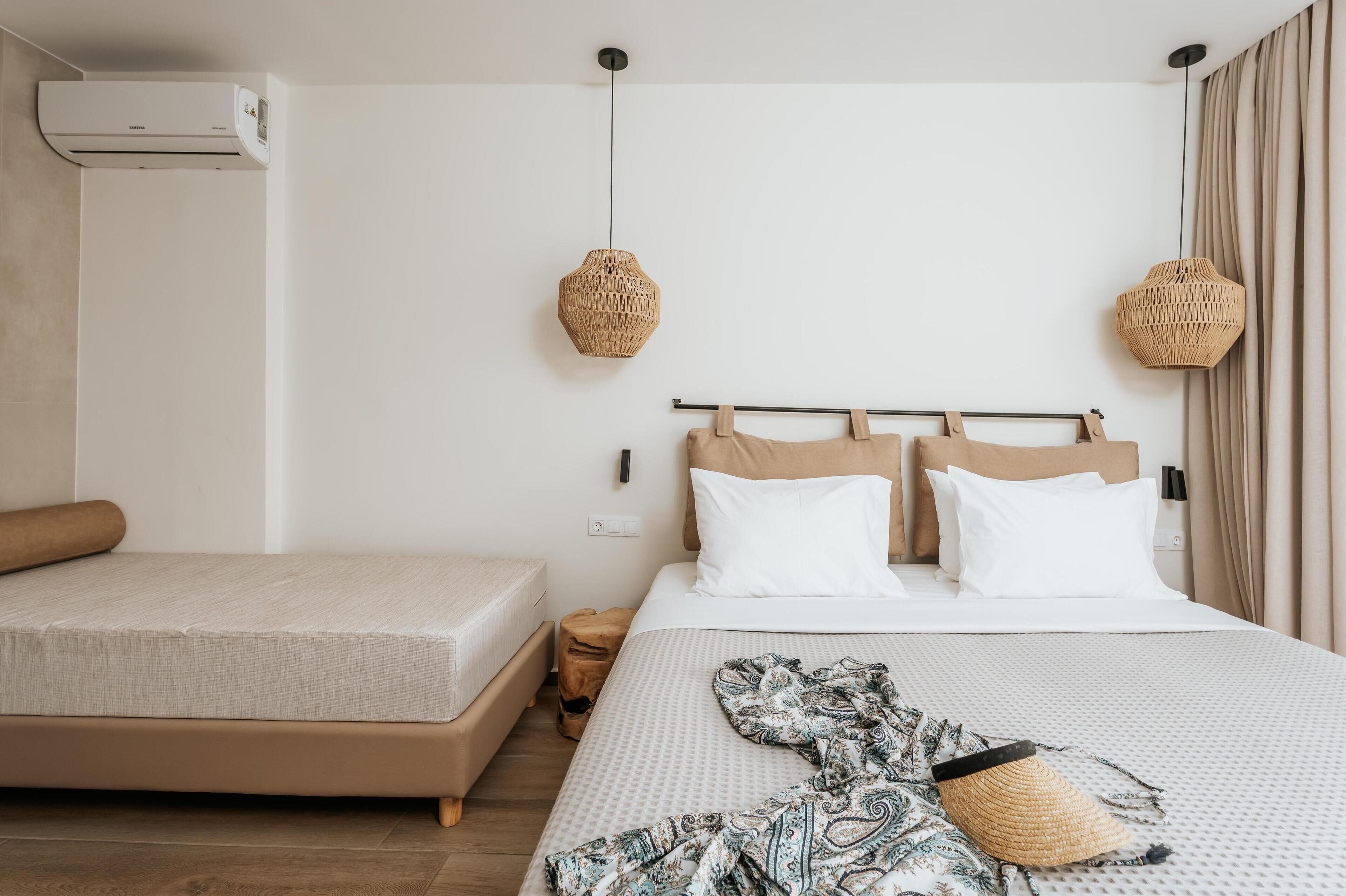 A bedroom with a bed, a smaller bed, a bedside table, a hanging light, and an air conditioning unit.