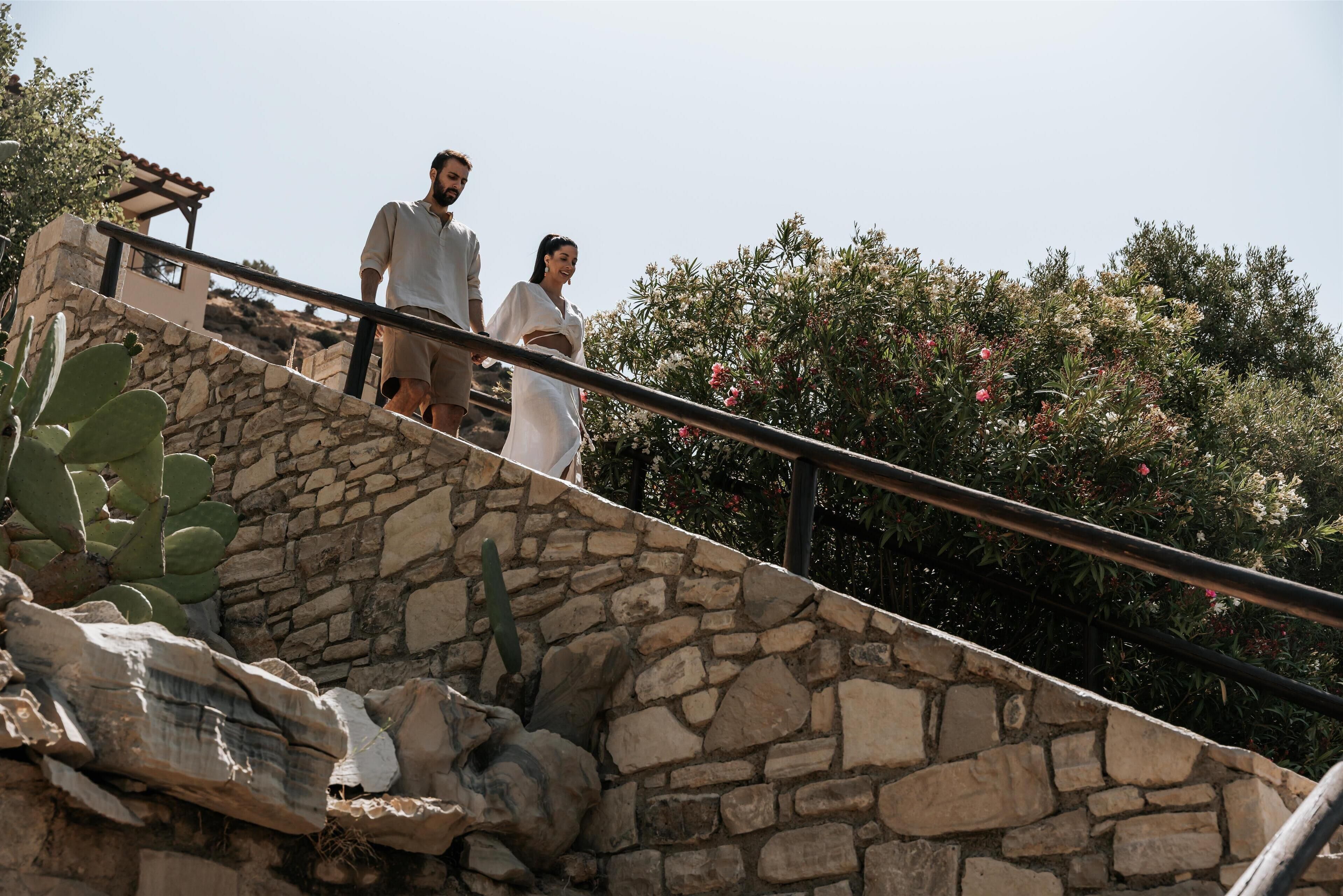 A stone staircase with a metal railing, surrounded by greenery and a clear sky.