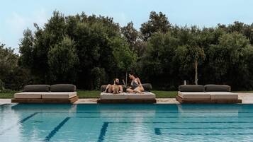 Un espace aménagé au bord de la piscine, comprenant deux chaises longues et un banc, le tout entouré de la piscine et d’une végétation luxuriante.