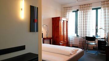 A hotel room with a bed, a desk, a chair, a wardrobe, and a window with curtains.