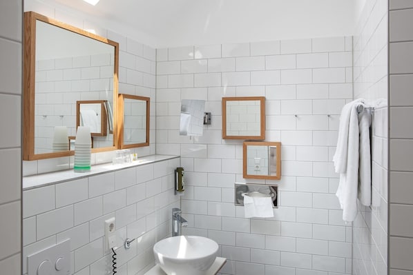 A modern bathroom with white tiles, a large mirror, a sink, and a towel rack. - DORMERO Hotel Kehl (Kehl)