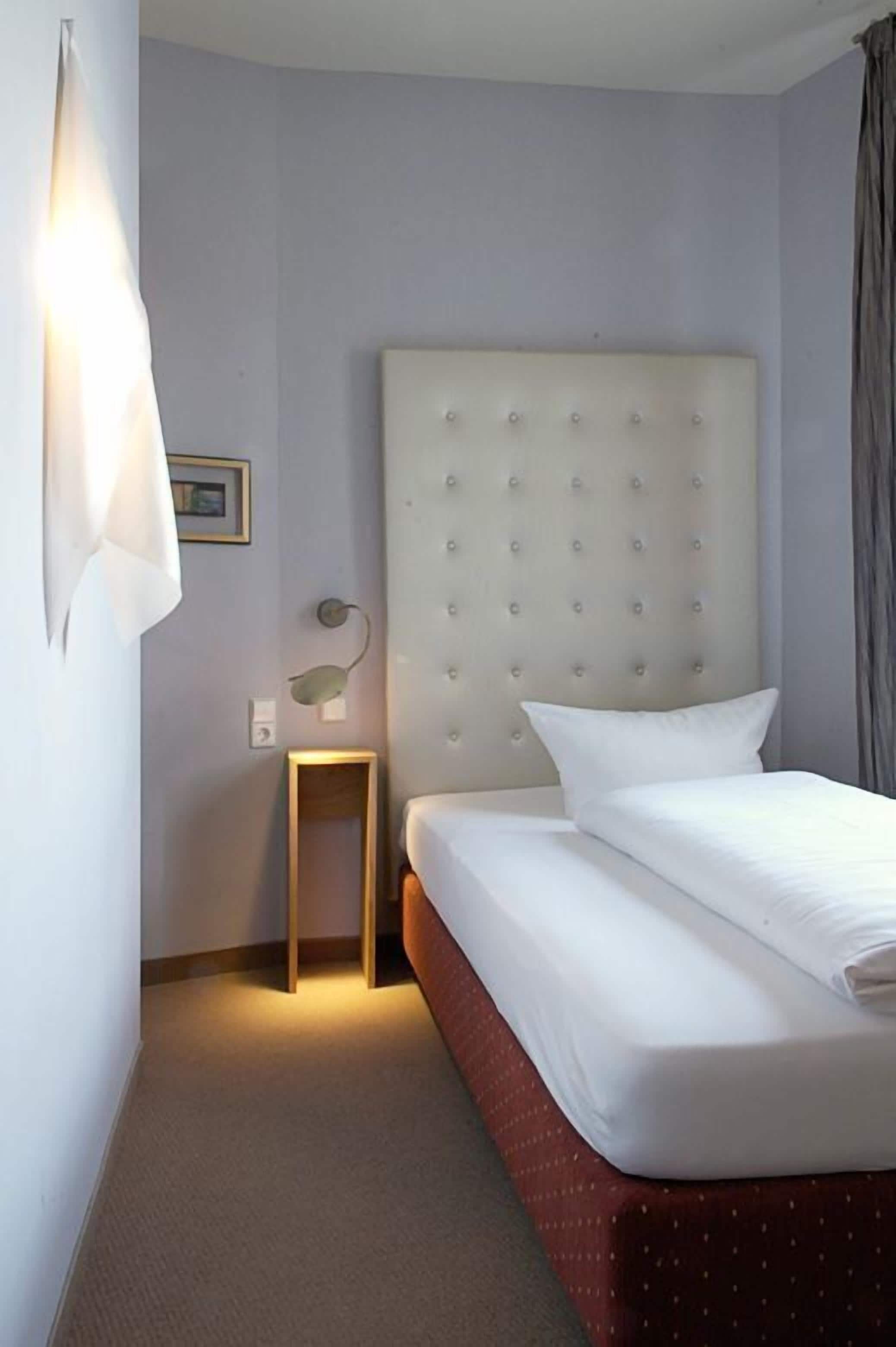A hotel room with a large bed, a headboard, a bedside table, and a wall-mounted lamp.
