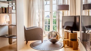 A living room with a sofa, a round rug, a television, and a bookshelf. - DORMERO Hotel Kehl (Kehl)