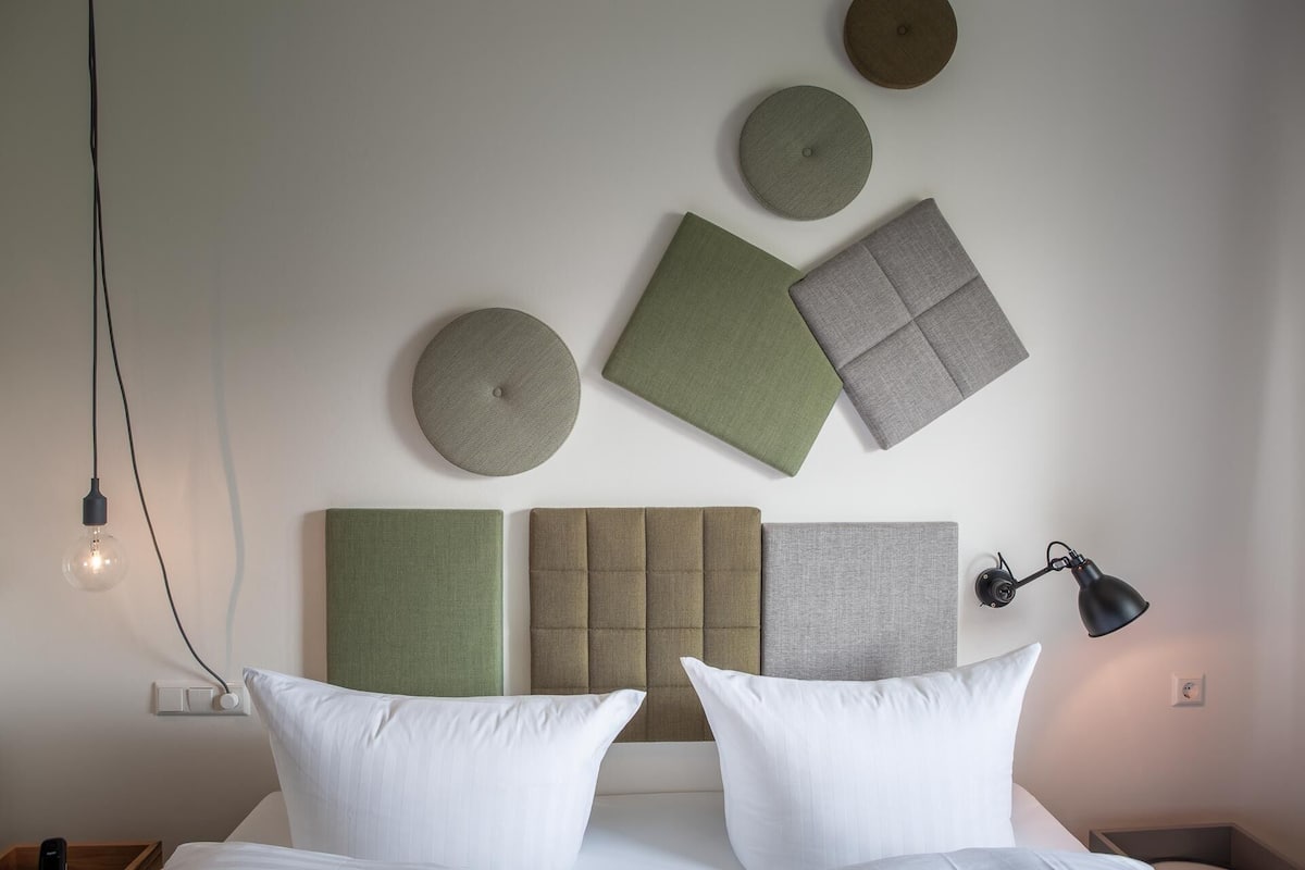 A neatly arranged bedroom with a bed, pillows, a wall-mounted lamp, and decorative wall pieces.