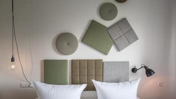 A neatly arranged bedroom with a bed, pillows, a wall-mounted lamp, and decorative wall pieces.