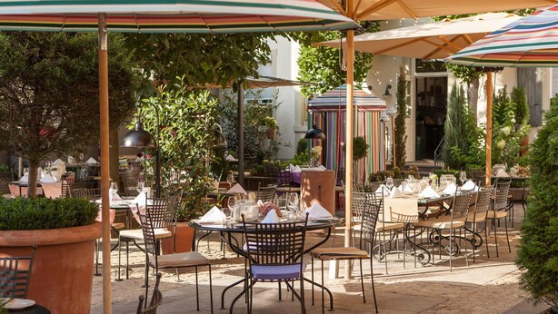 An outdoor dining area with tables and chairs, umbrellas, and potted plants. - DORMERO Hotel Kehl (Kehl)