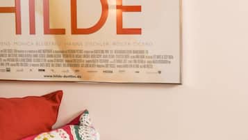 En inramad filmplakat för filmen ”MAKATSCH HILDE” hänger på väggen, och under den finns två dekorativa kuddar.