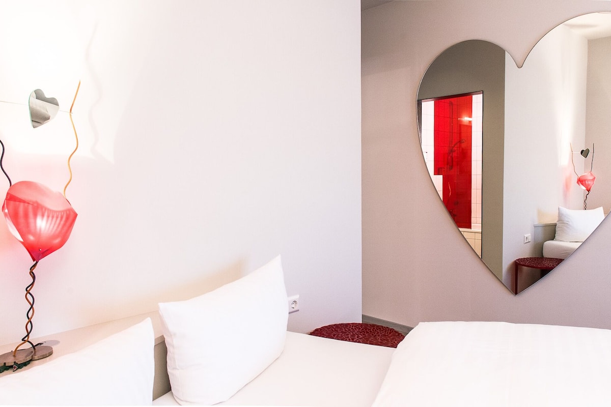 A hotel room with a bed, a heart-shaped mirror, and a red balloon.