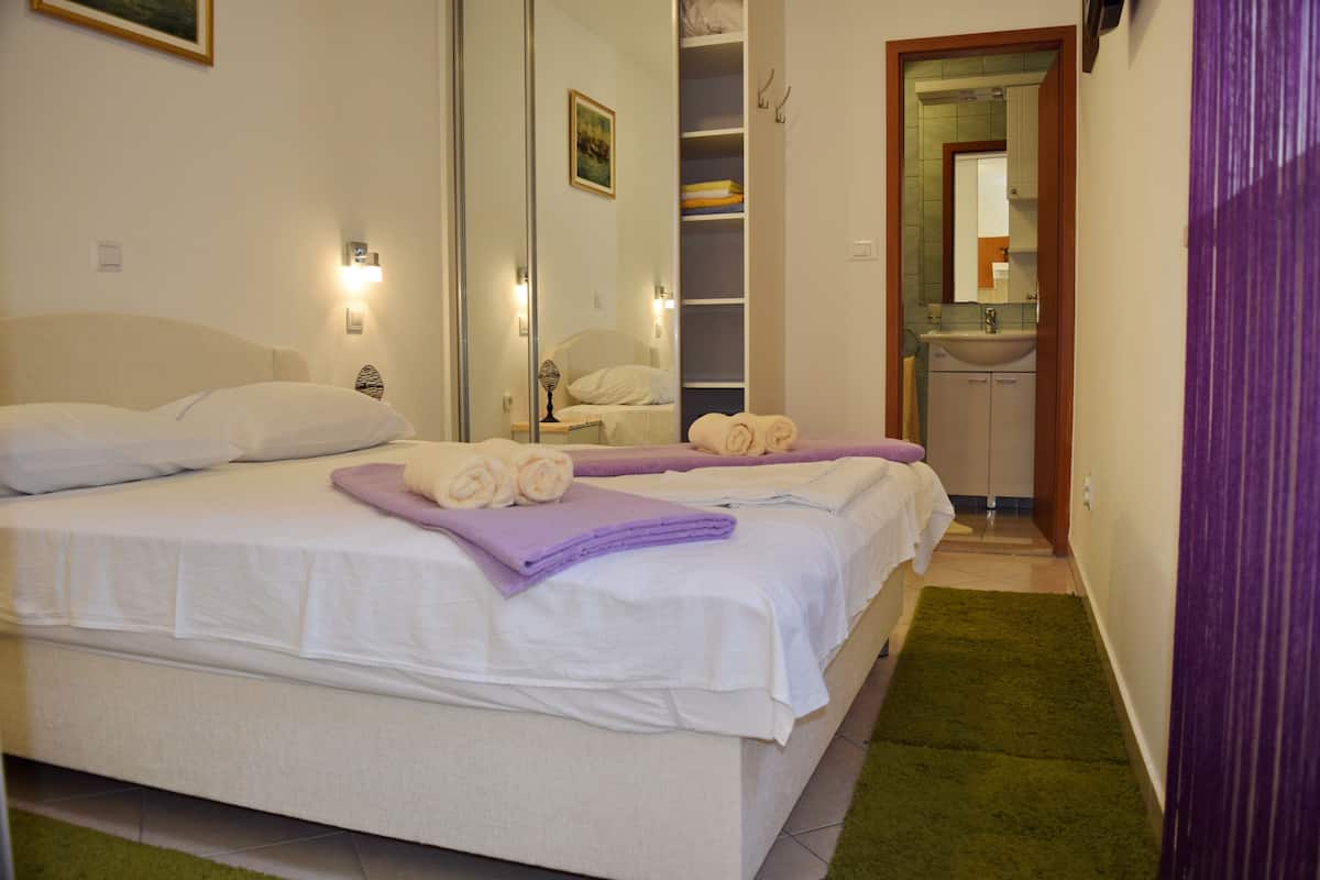 A hotel room with a large bed, a mirror, a bathroom with a sink, and a green carpet.