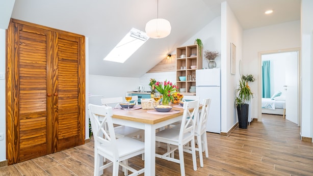 A dining area with a wooden table, white chairs, and a ceiling light. - Jele Rooms (Dubrovnik)