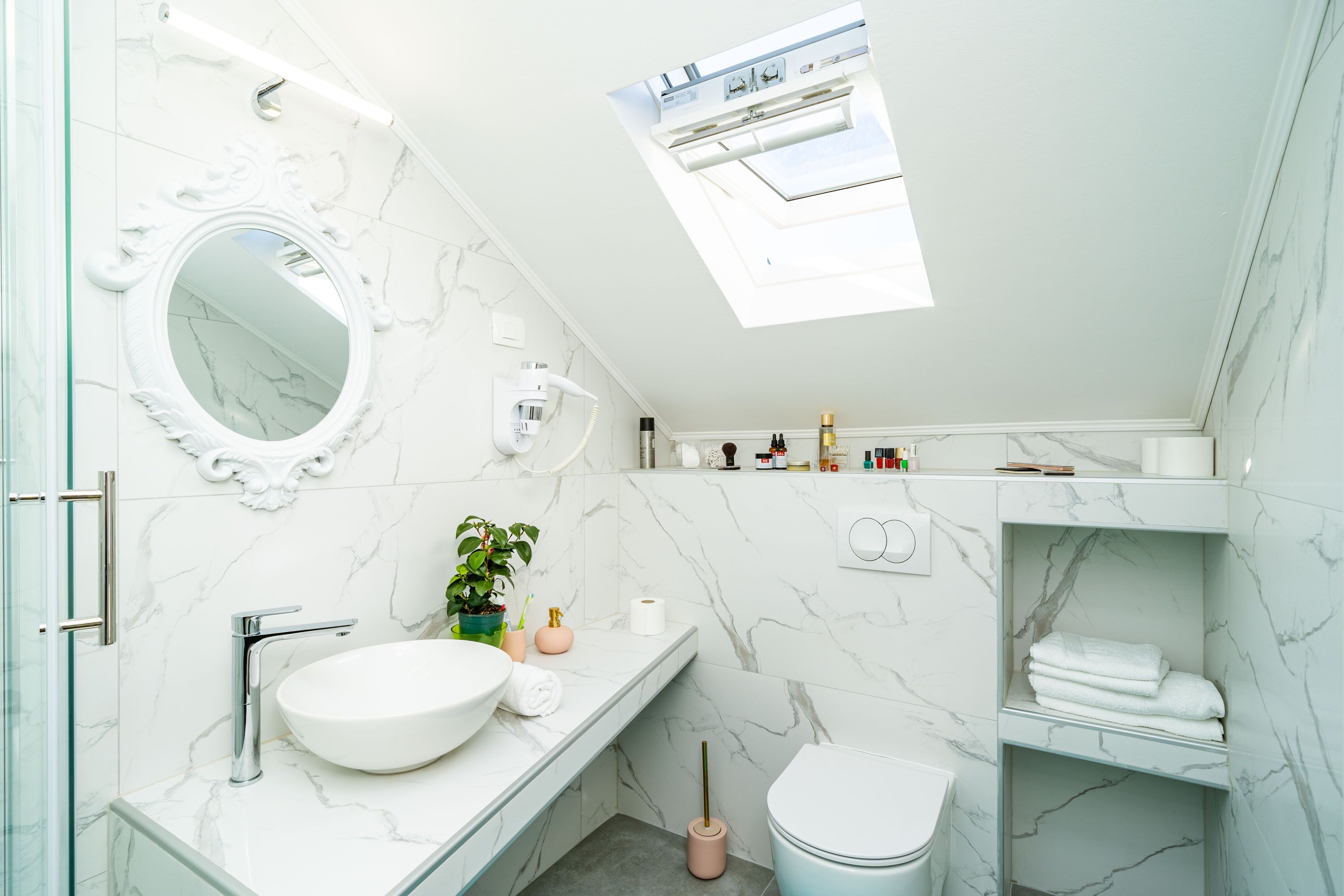 A modern bathroom with a skylight, a round mirror, a white sink, and a toilet.