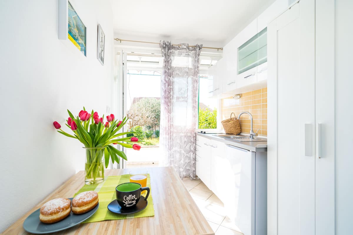 A narrow kitchen with a window, a vase with tulips, a coffee cup, and a plate with pastries.