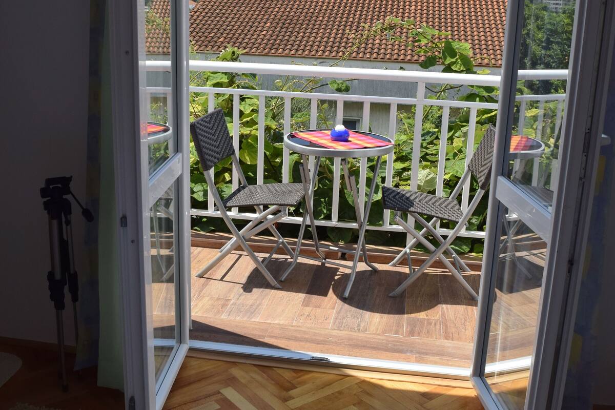 A balcony with a view of a cityscape, a table with chairs, and a bed with towels.