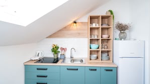 A modern kitchen with a skylight, wooden shelves, a white refrigerator, and teal cabinets. - Jele Rooms (Dubrovnik)