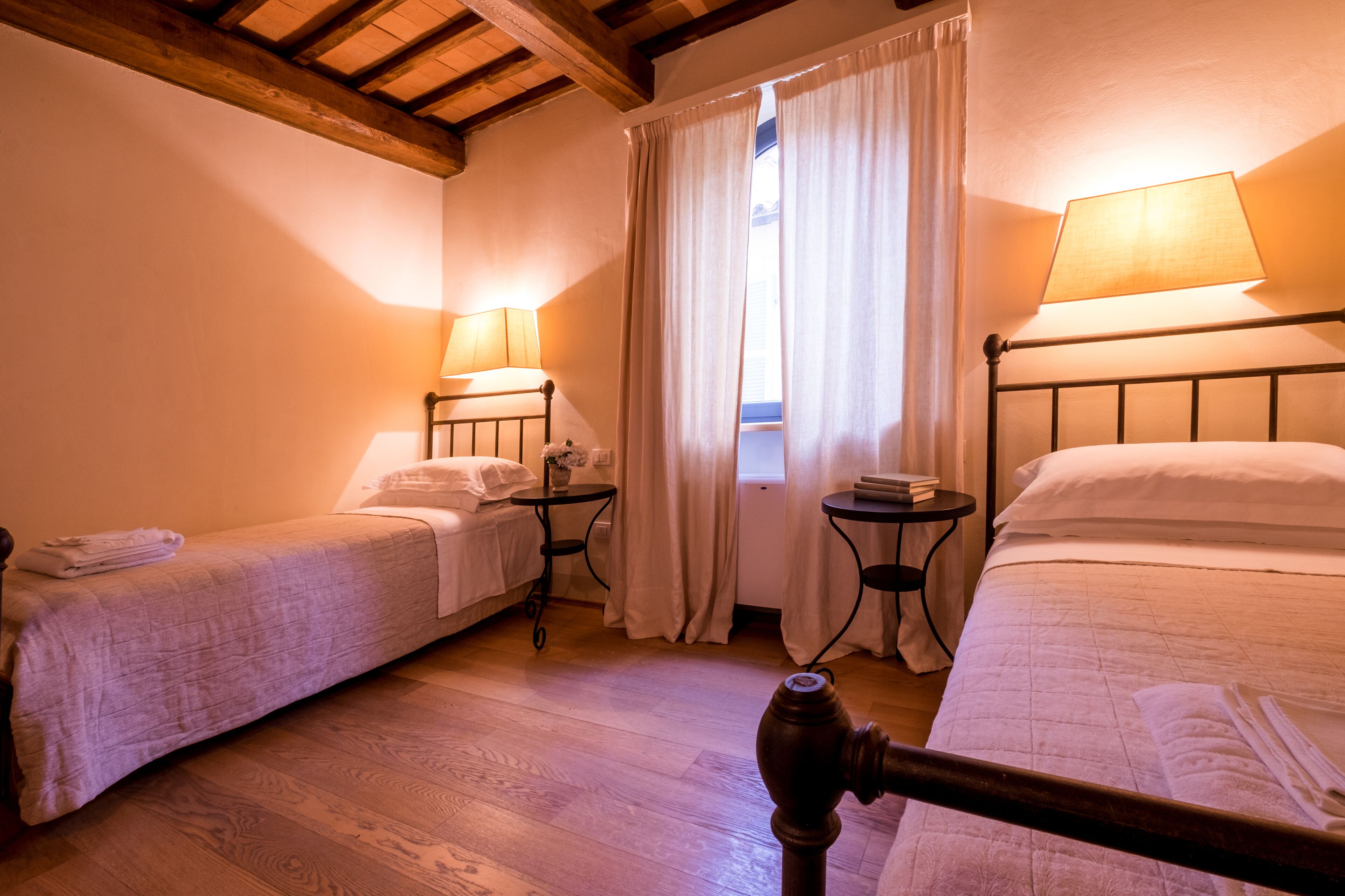 Une chambre avec deux lits simples, une petite table, une fenêtre avec des rideaux et une lampe sur chaque lit.