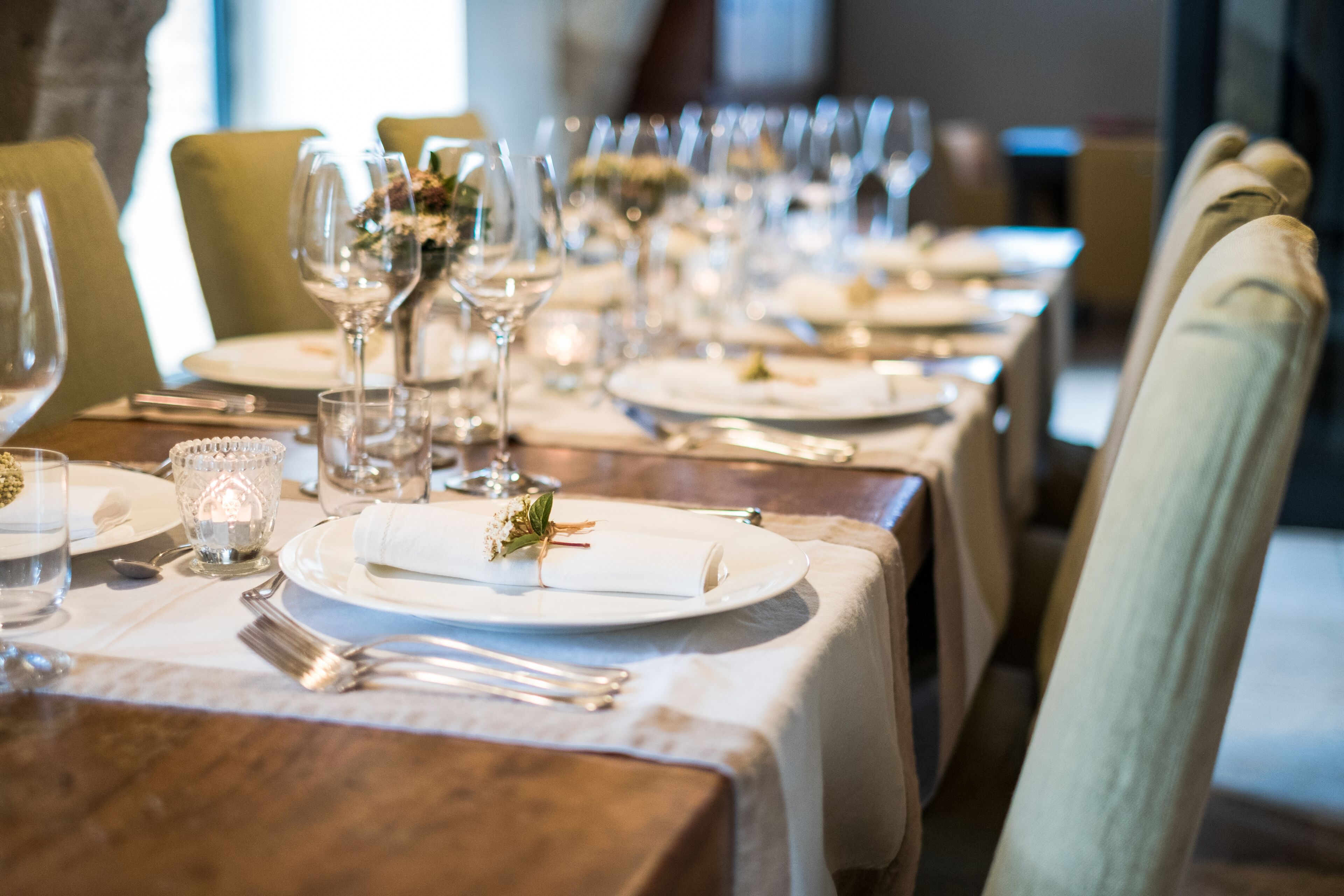 A dining table set with plates, cutlery, and glasses, with a candle and a flower centerpiece.