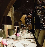 Una larga mesa de comedor preparada con múltiples copas de vino, platos y cubiertos, con sillas a cada lado.