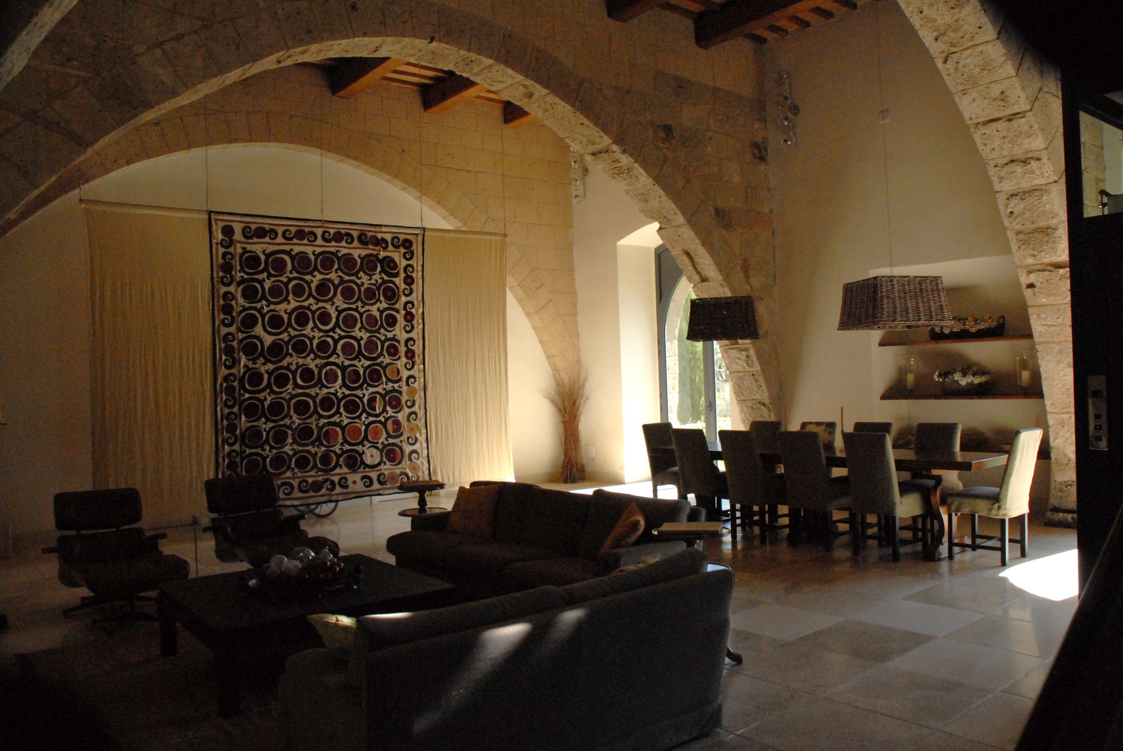 Amplia sala de estar con un arco de piedra, un panel decorativo grande y un comedor con sillas y mesas.