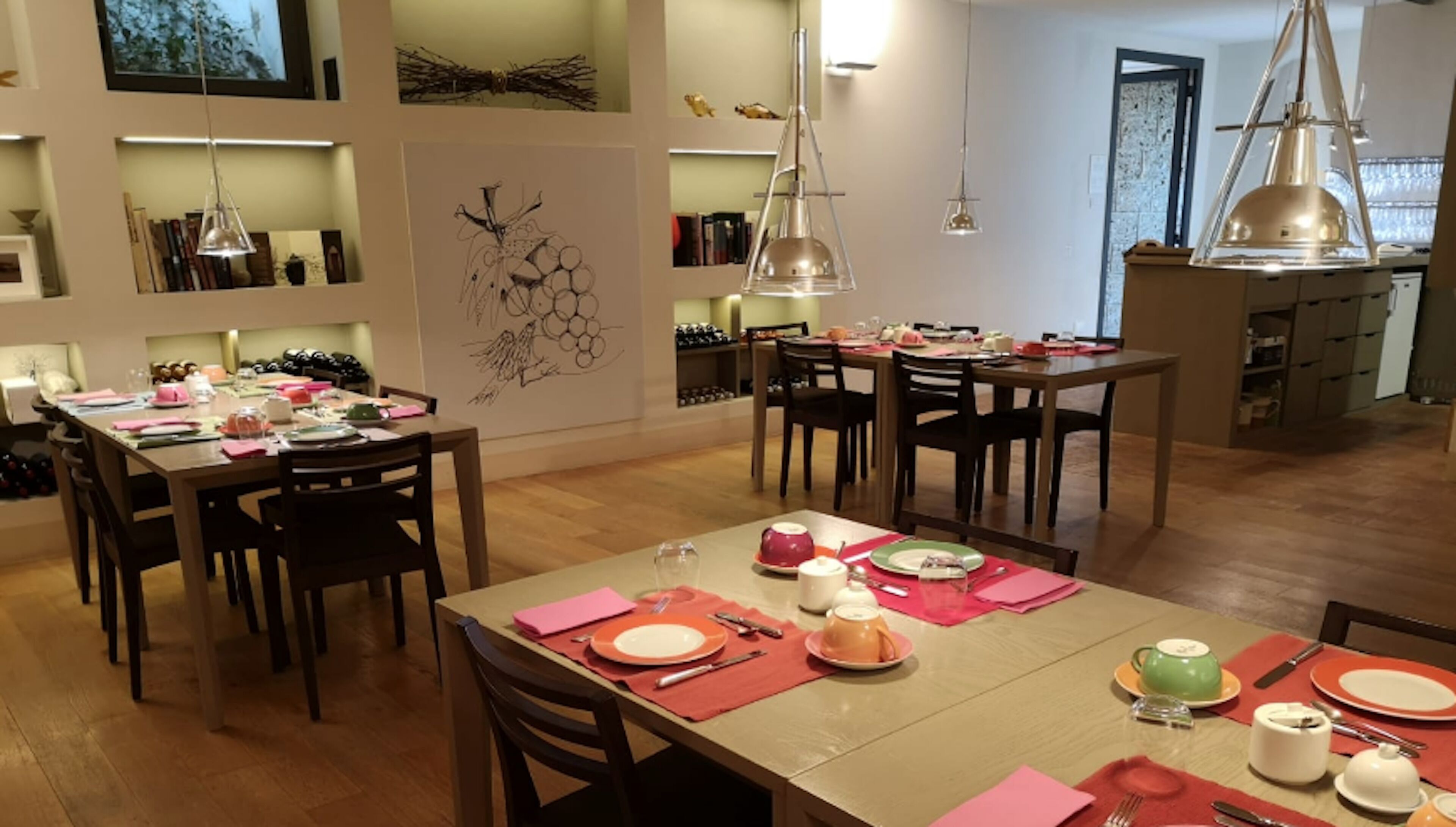 Un espace repas avec plusieurs tables dressées pour les repas, des chaises en bois et des luminaires suspendus.