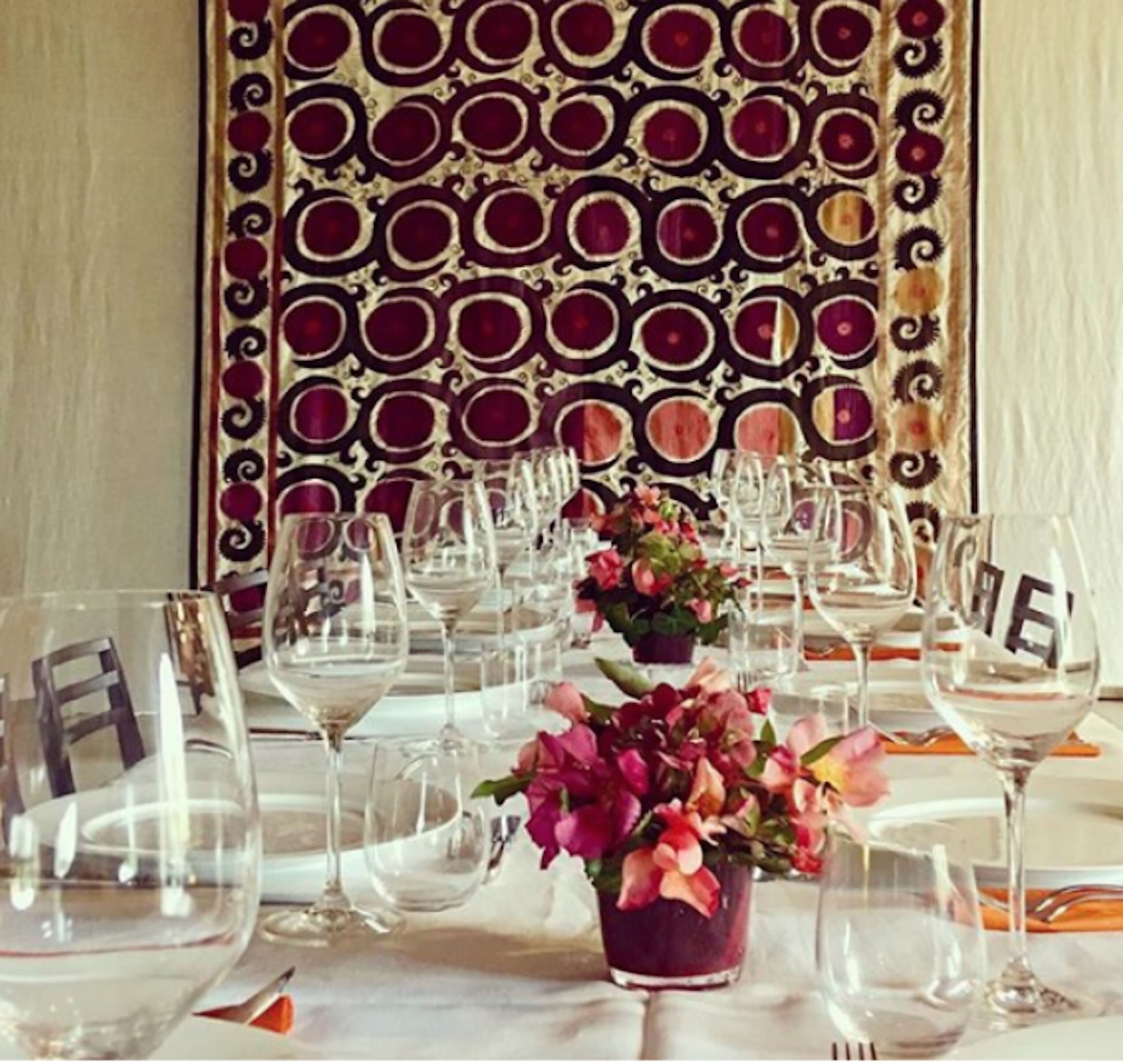 Mesa dispuesta para una ocasión de cena formal, con cristalería transparente y una pared decorativa al fondo.