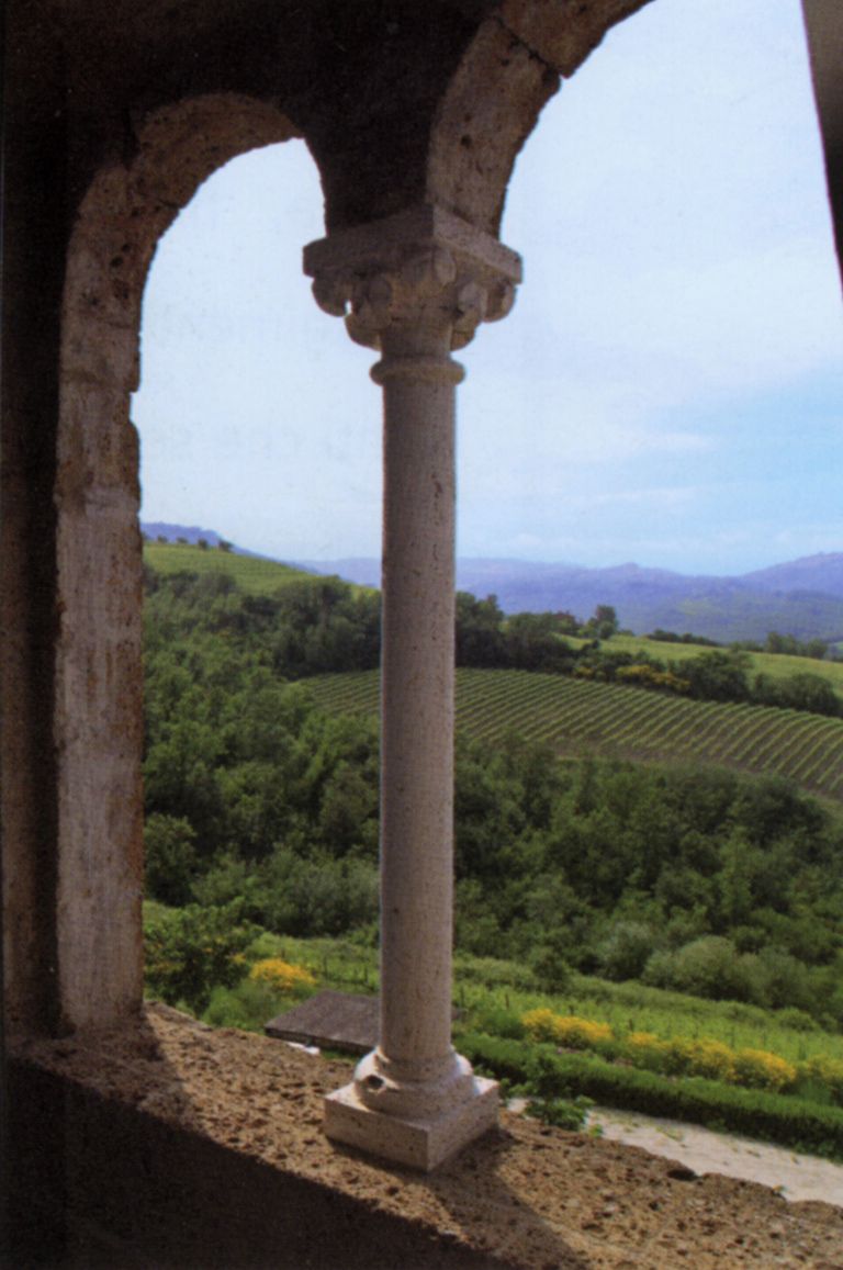 A stone column within an arched structure, overlooking a lush green landscape with terraced fields.