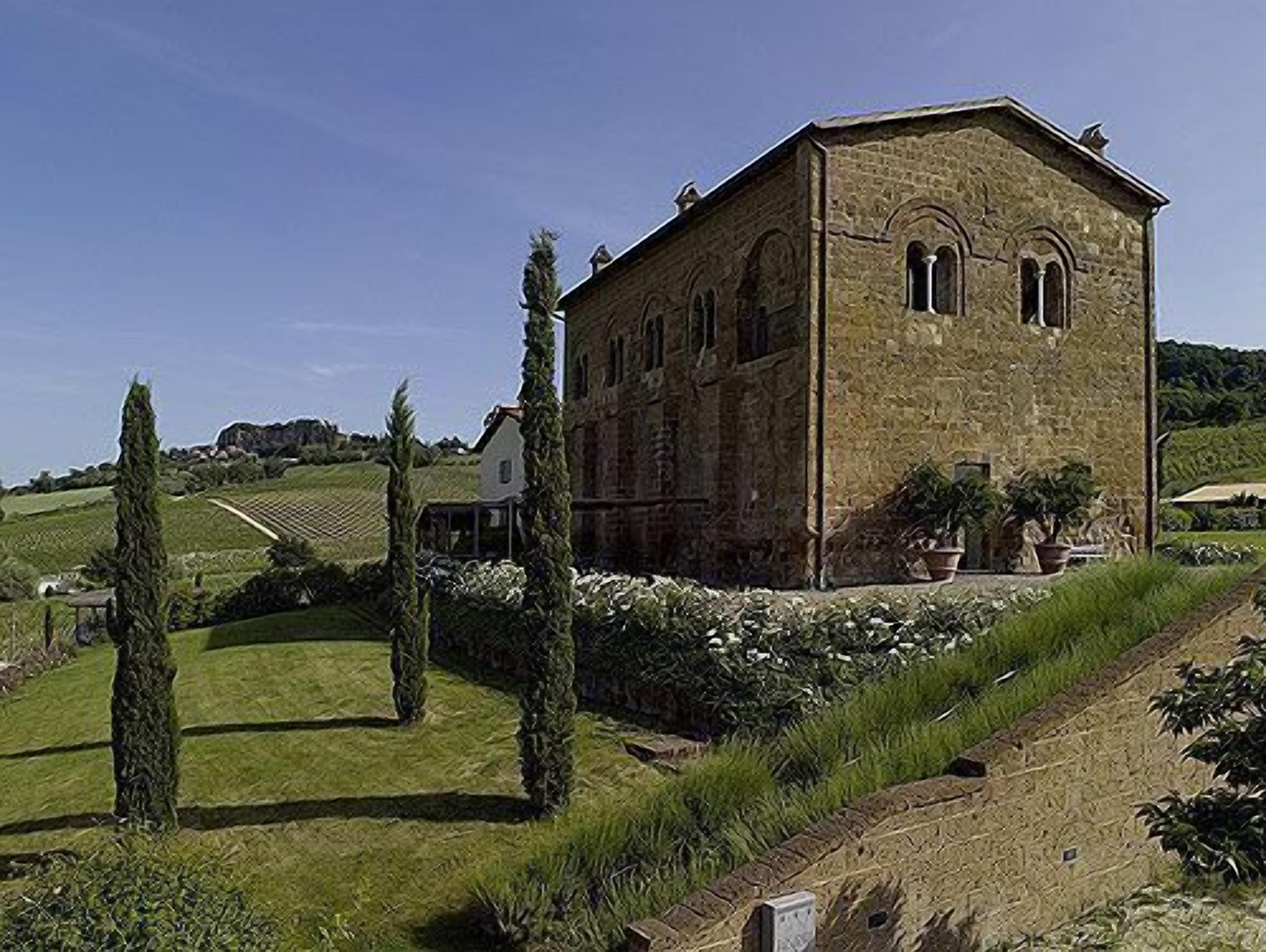 A stone building with arched windows, surrounded by greenery and a sloped landscape.
