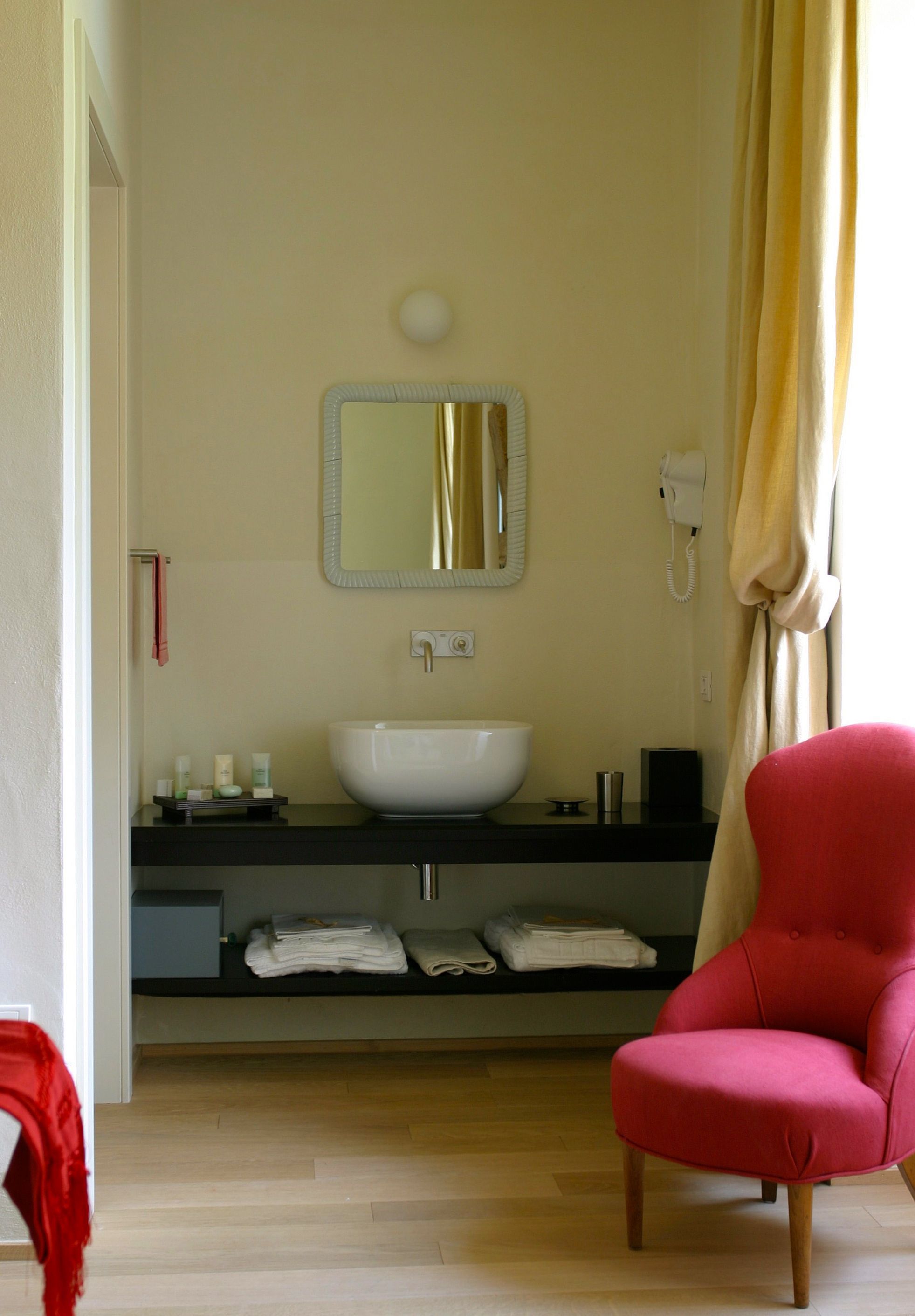A bathroom with a white sink, a mirror, a telephone, and a red chair.