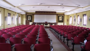 Een congrescentrum met rijen rode stoelen, een groot projectiescherm en een spreekgestalte vooraan.