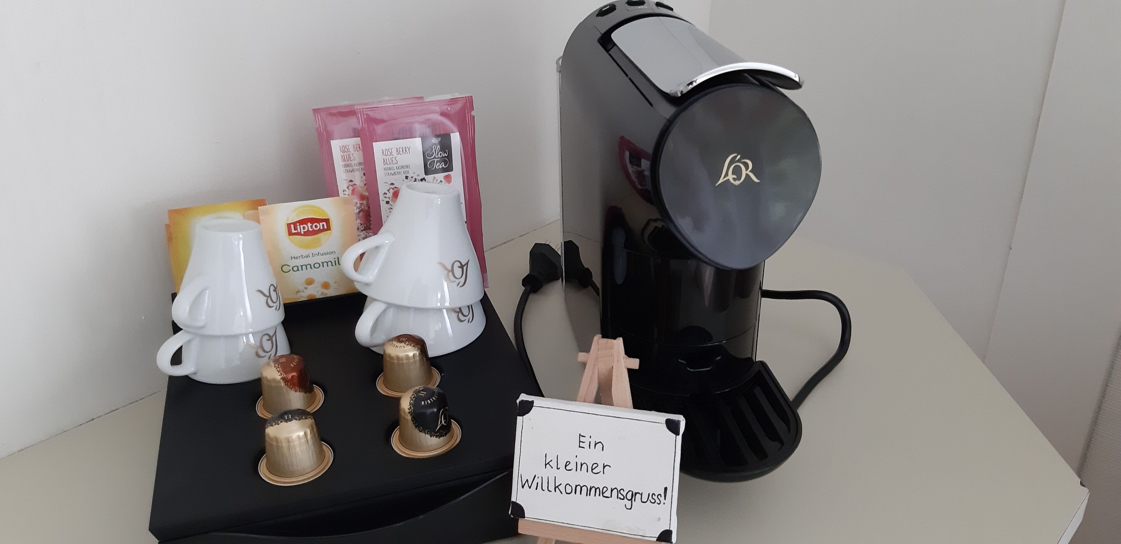 A coffee machine, a white teapot, Lipton tea bags, and a sign in German.