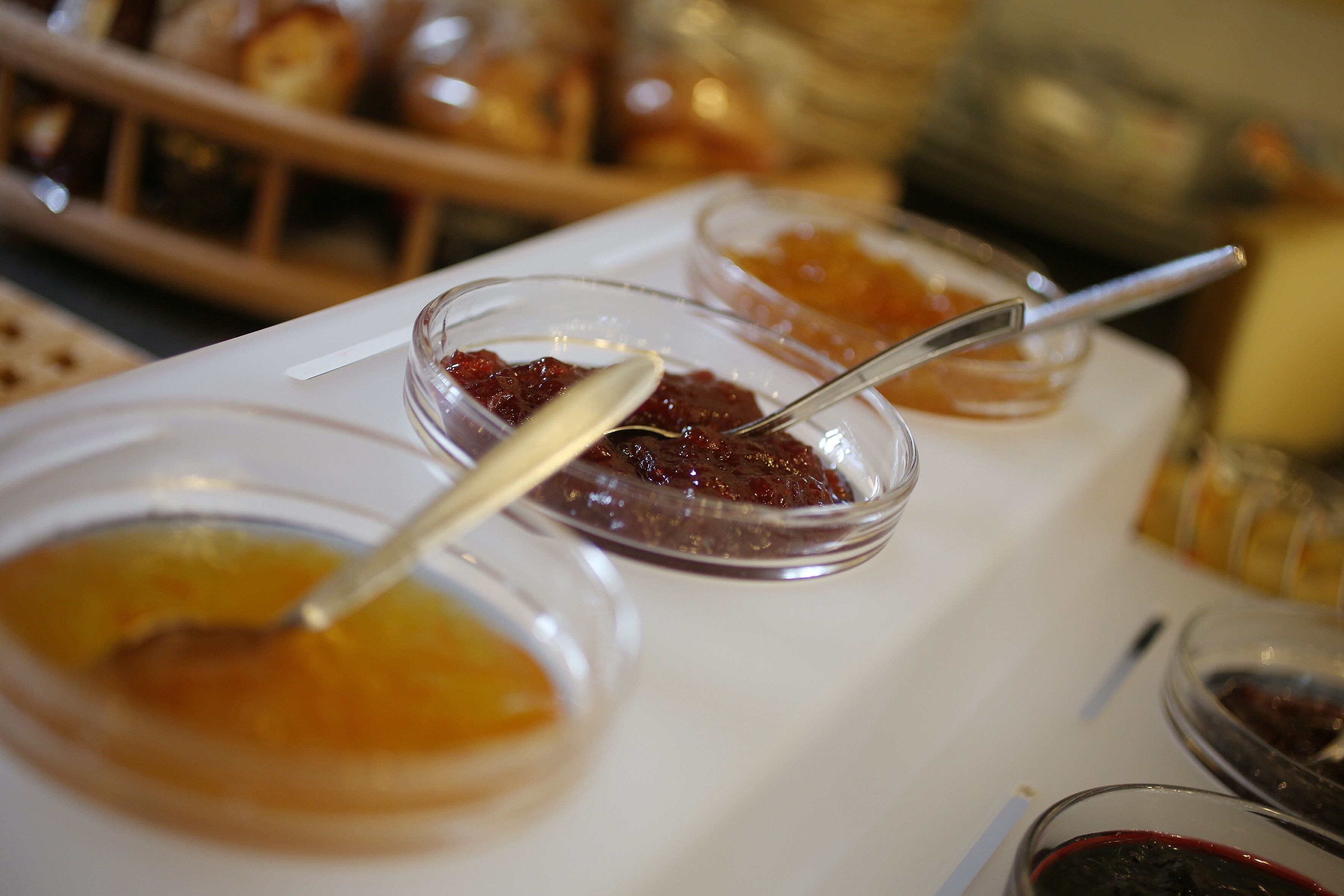 Une table de buffet avec divers aliments présentés dans des récipients transparents, notamment des confitures et des sauces.