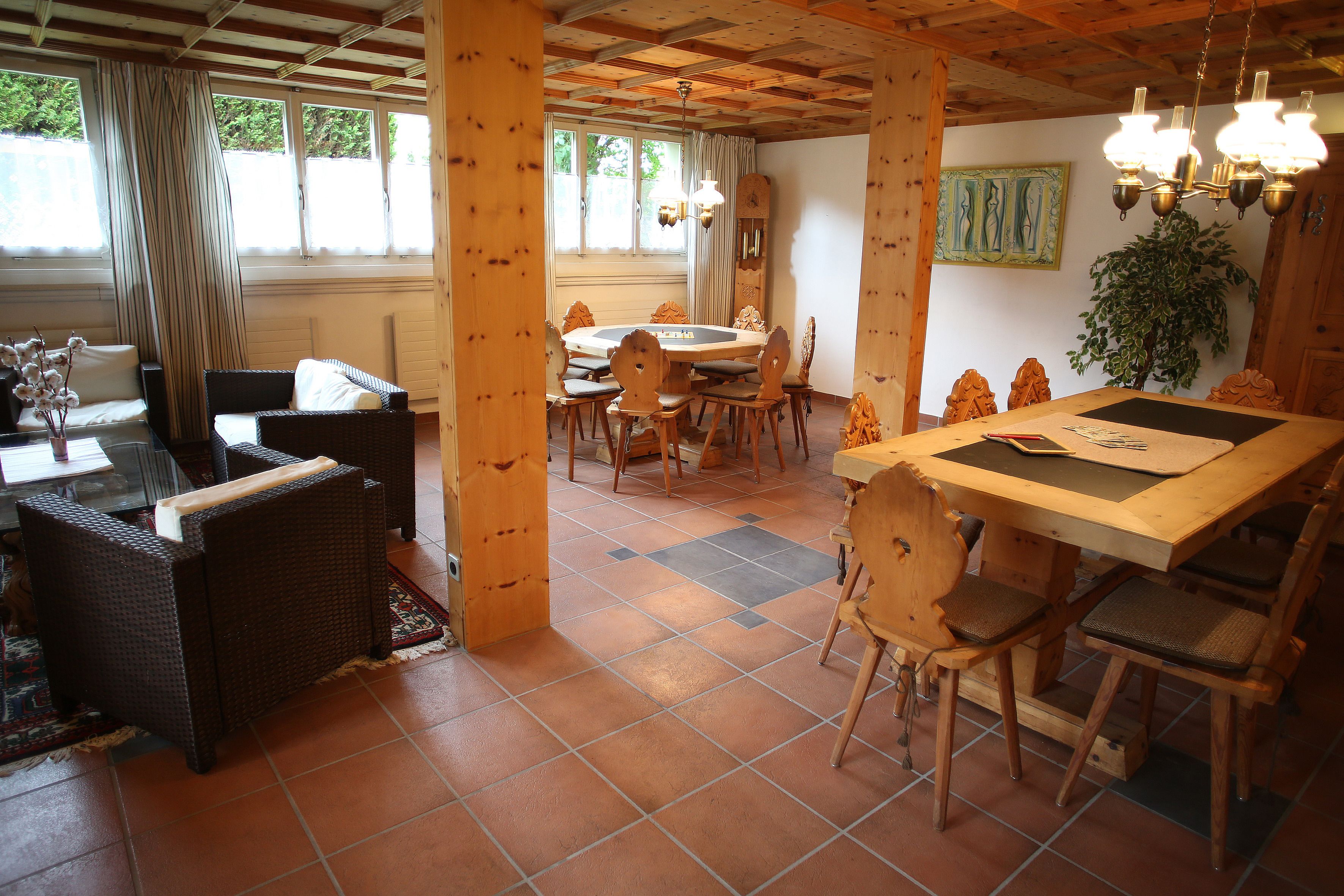 A dining area with a round table, chairs, and a view of the outdoors through large windows.