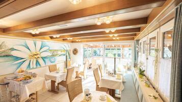 A restaurant with wicker chairs, white tablecloths, and a mural on the wall.