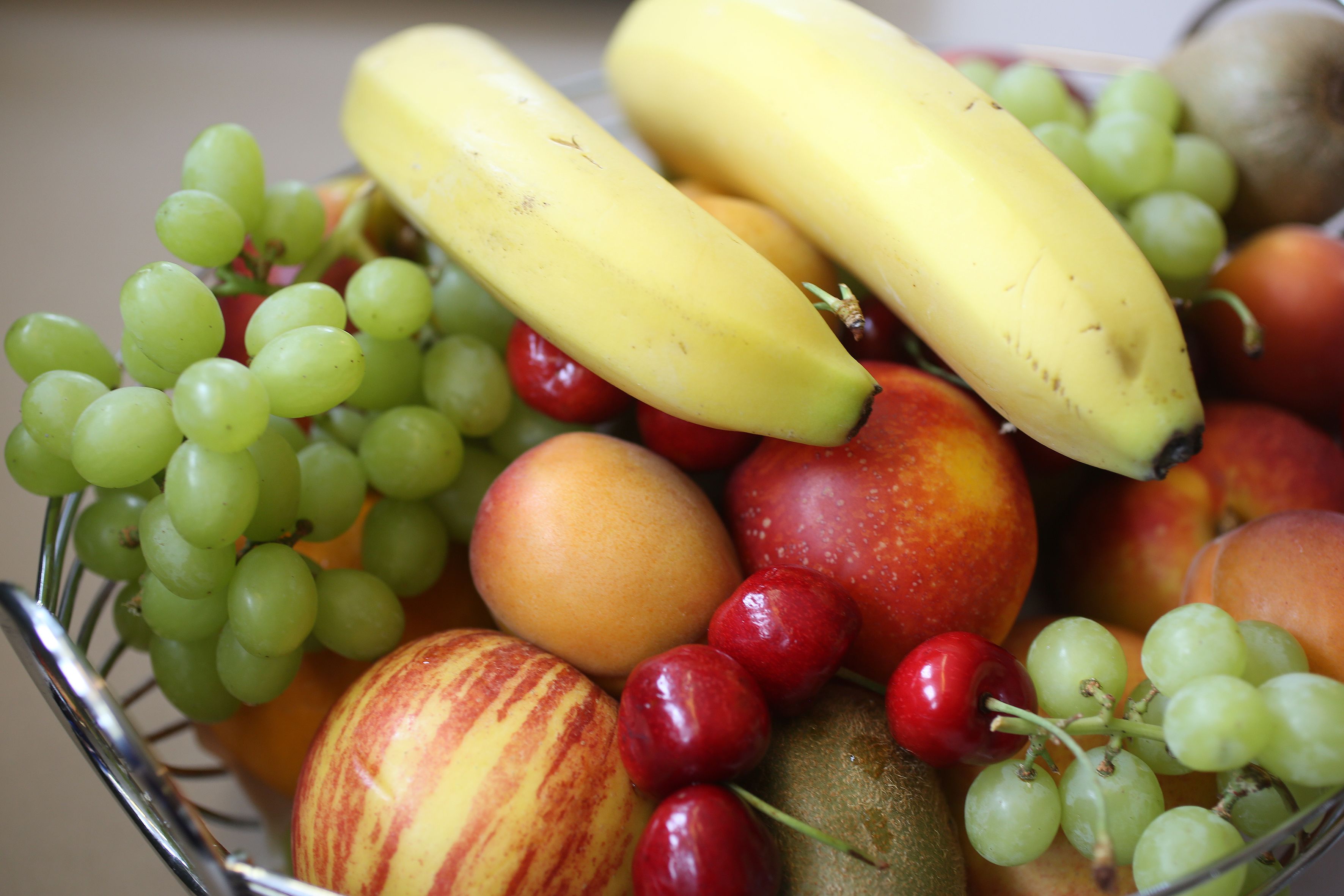 A fruit bowl containing bananas, apples, grapes, and cherries.