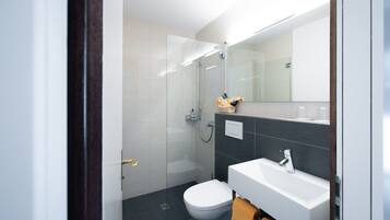 Uma casa de banho moderna com cabine de duche em vidro, sanita branca e lavatório branco com uma toalha pendurada ao lado.